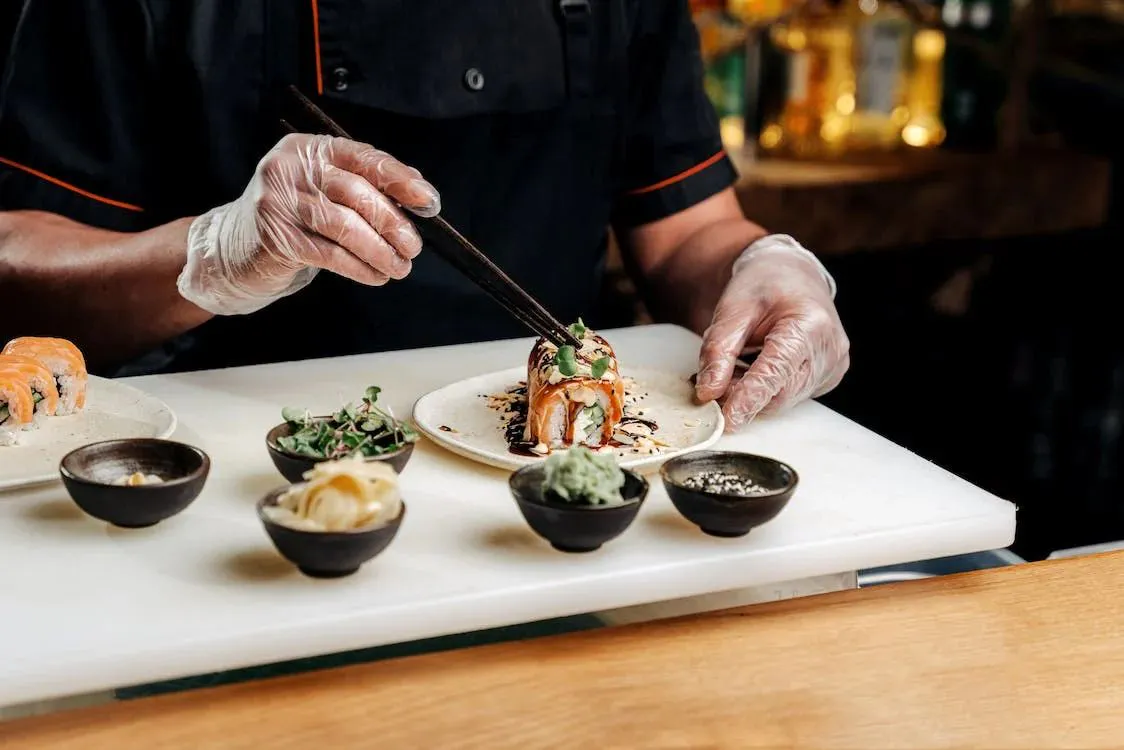 Sushi chef carefully garnishing a freshly prepared sushi roll with chopsticks